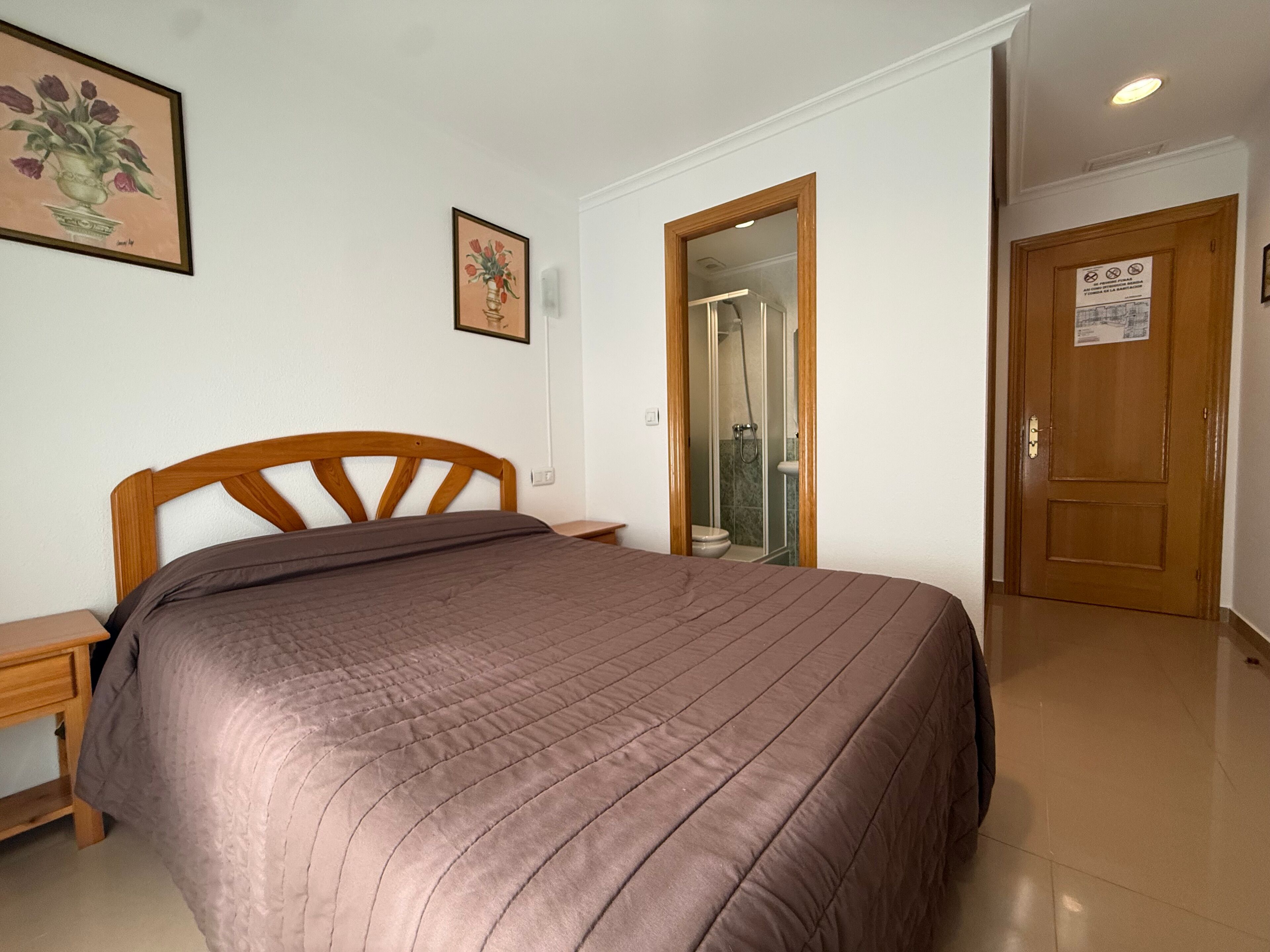 Une chambre à coucher avec un lit en bois, une table de chevet et une œuvre d’art florale encadrée accrochée au mur.