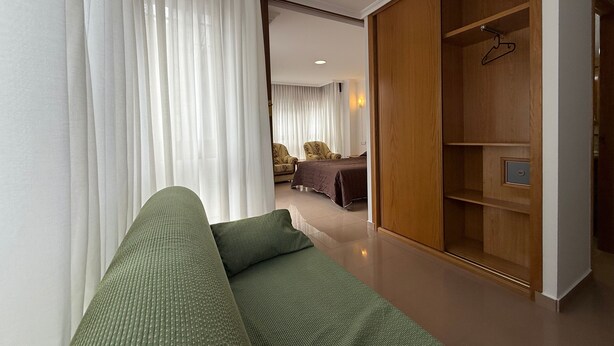 Une chambre d’hôtel moderne avec un canapé vert, une armoire en bois et un lit recouvert d’une courtepointe marron.