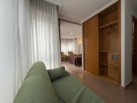 Una habitación de hotel moderna con un sof á verde, un armario de madera y una cama con colcha marrón.
