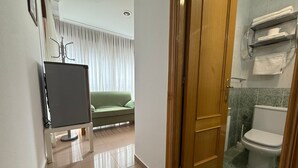 Une chambre d’hôtel avec un canapé vert, une porte en bois et une salle de bain équipée de toilettes et d’un porte-serviettes.
