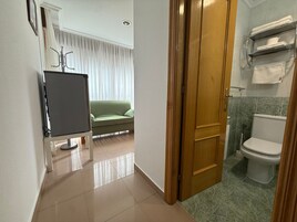 Habitación de hotel con sofá verde, puerta de madera y baño con inodoro y toallero.