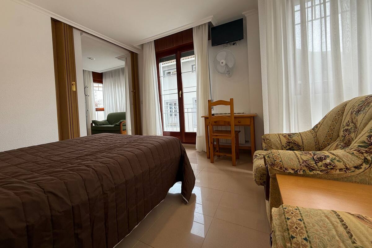A hotel room with a bed, a chair, a desk, and a TV mounted on the wall.