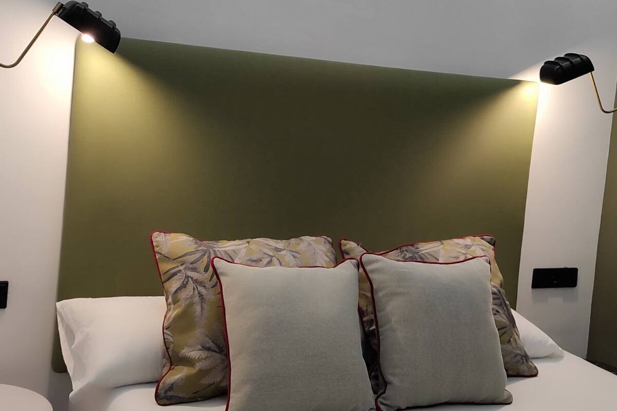 Una habitación de hotel moderna con una cama, dos lámparas de noche, una mesita redonda y una pared de acento verde.