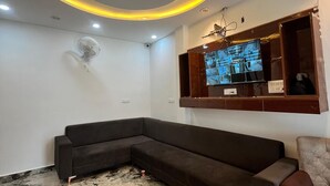 A modern living room with a curved ceiling light, a sectional sofa, a flat-screen TV, and a marble floor. - Hotel Golden Palace (Agra)