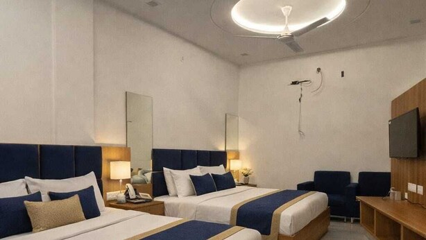 A hotel room with two beds, a desk, a chair, a TV, and a ceiling fan. - Hotel Golden Palace (Agra)