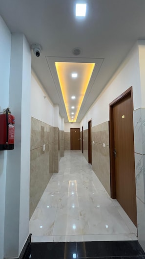 A hallway with a fire extinguisher on the left, a ceiling light, and a door at the end. - Hotel Golden Palace (Agra)