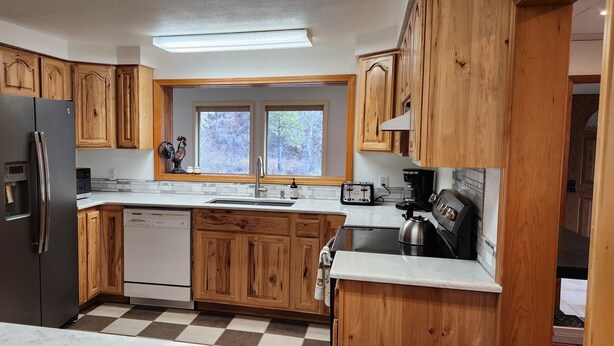 A kitchen with wooden cabinets, a black refrigerator, a dishwasher, a window, and a coffee maker. - House right on Pine Creek, only one mile from the Snake. (Oxbow)