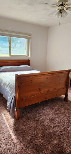 Un dormitorio con cama de madera, ventilador de techo y ventana con vistas al exterior.