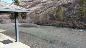 A gravel area with a metal shelter and a river in the background. - House right on Pine Creek, only one mile from the Snake. (Oxbow)