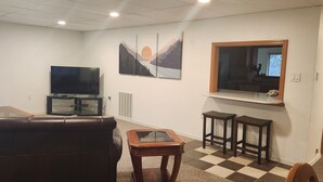 A living room with a leather couch, a glass coffee table, a flat-screen TV, two wooden stools, and a window with a view of mountains. - House right on Pine Creek, only one mile from the Snake. (Oxbow)