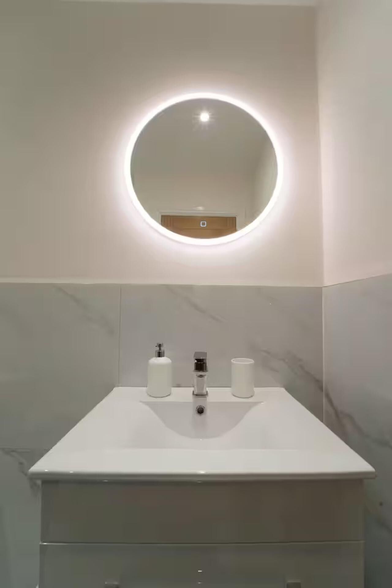 A modern bathroom with a round mirror, white sink, and marble tiles.