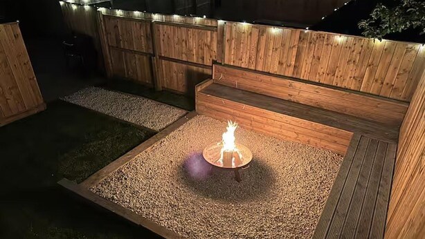 Un foyer est entouré d’une terrasse en bois, et un espace recouvert de gravier se trouve au centre.