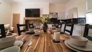 Un coin repas avec une table en bois, dressée pour quatre personnes, entourée de chaises. Un vase rempli de fleurs est placé au centre.