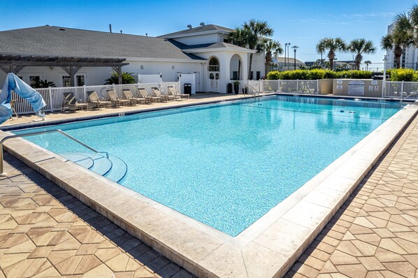 A rectangular swimming pool with a tiled deck, lounge chairs, and a white building with a grey roof in the background. - Spacious 2 bedroom w/Beach Service ST 3114 (Destin)