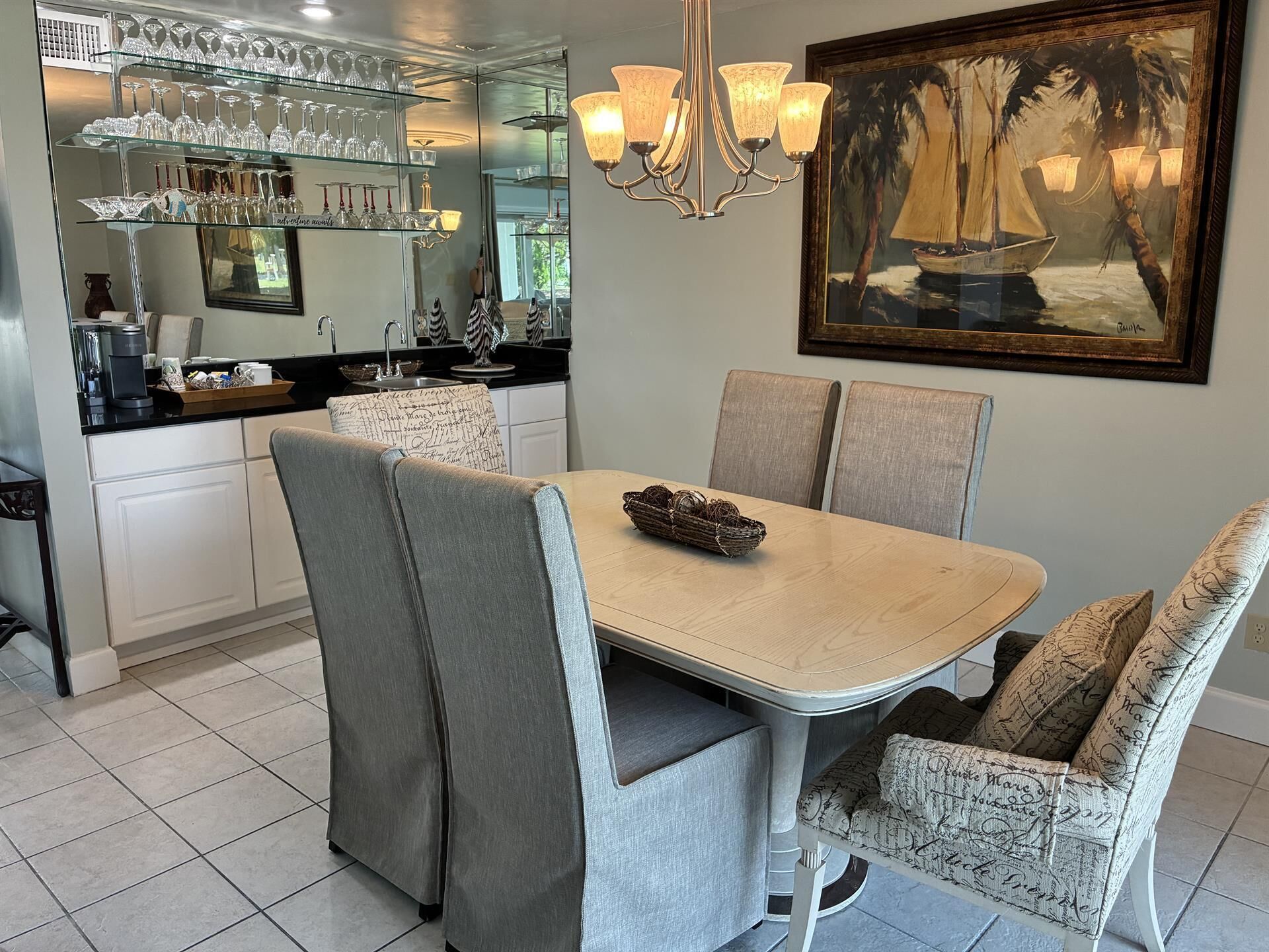 Un'area pranzo con tavolo e sedie, un lampadario, un quadro e una cucina sullo sfondo.