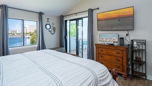 Ein Schlafzimmer mit einem großen Bett, einer Kommode, einem Fernseher und Blick auf die Stadt durch das Fenster.