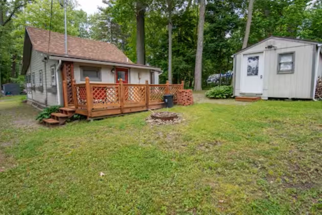 A small house with a porch and a shed in a grassy yard.