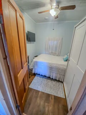 A bedroom with a bed, a ceiling fan, a TV, and a wooden door. - Cozy Cottage on Silver lake (Castile)