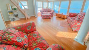 Ein geräumiges Zimmer mit Holzboden, großen Fenstern und einem roten, floralen Sofa.