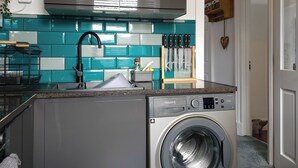 A compact kitchen with a built-in washing machine, a stainless steel range hood, and a teal backsplash. - Stunning, large, 2 king sized bedroom apartment. (Glasgow)