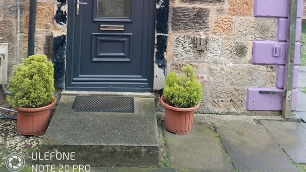 A dark blue door with the number 102, set in a stone building with a purple mailbox and two potted plants on the steps. - Stunning, large, 2 king sized bedroom apartment. (Glasgow)