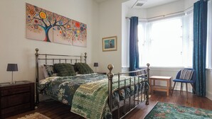 A bedroom with a bed, a desk, a chair, a window with curtains, and artwork on the walls. - Stunning, large, 2 king sized bedroom apartment. (Glasgow)