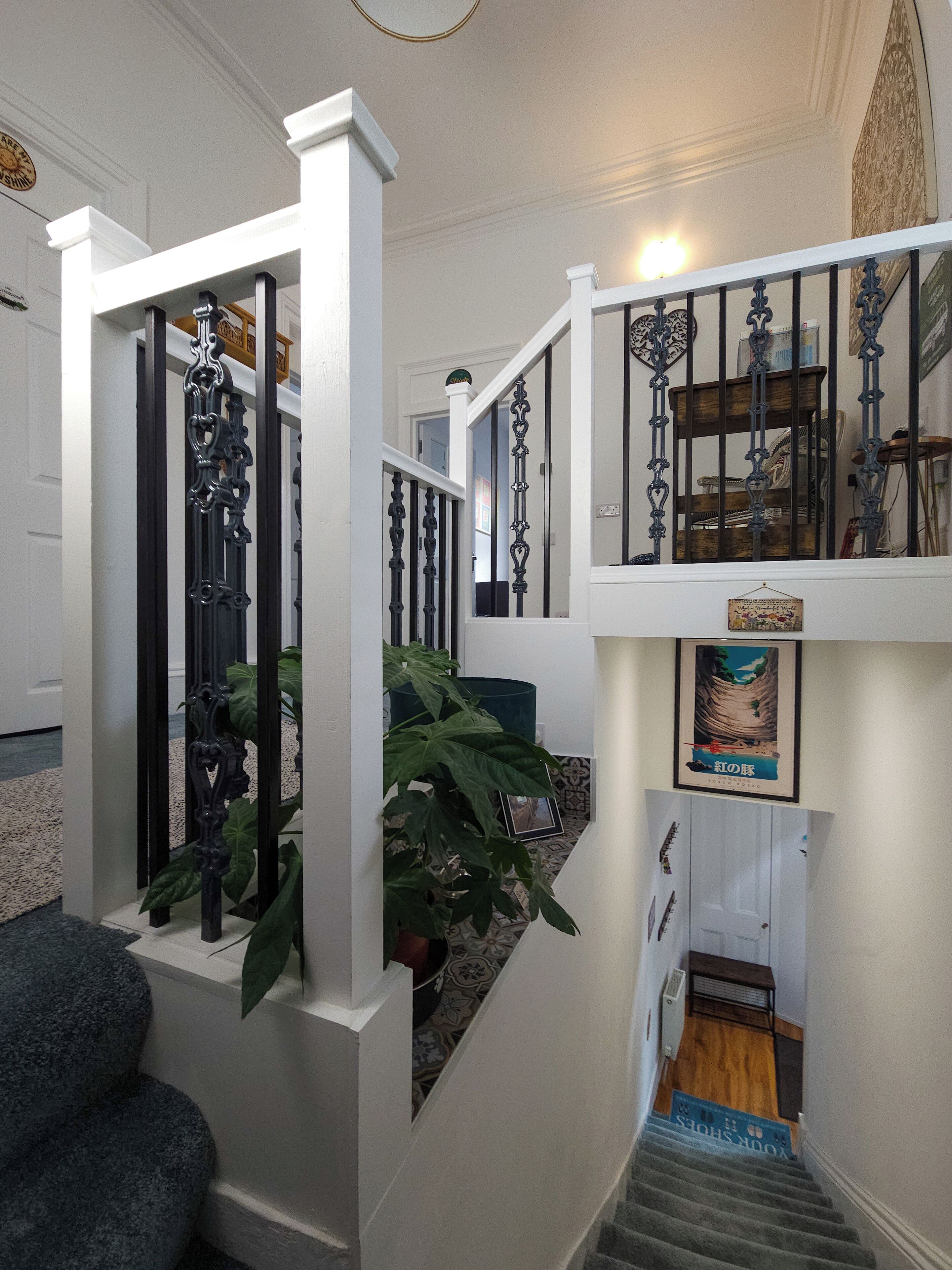 A staircase with ornate black railings, a potted plant, and a framed picture on the wall.