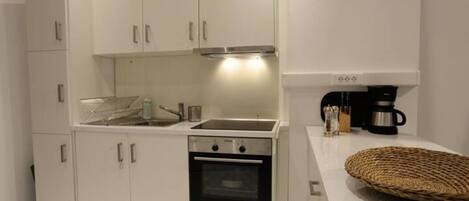 A modern kitchen with white cabinets, a stainless steel sink, a built-in oven, and a coffee maker on the countertop.