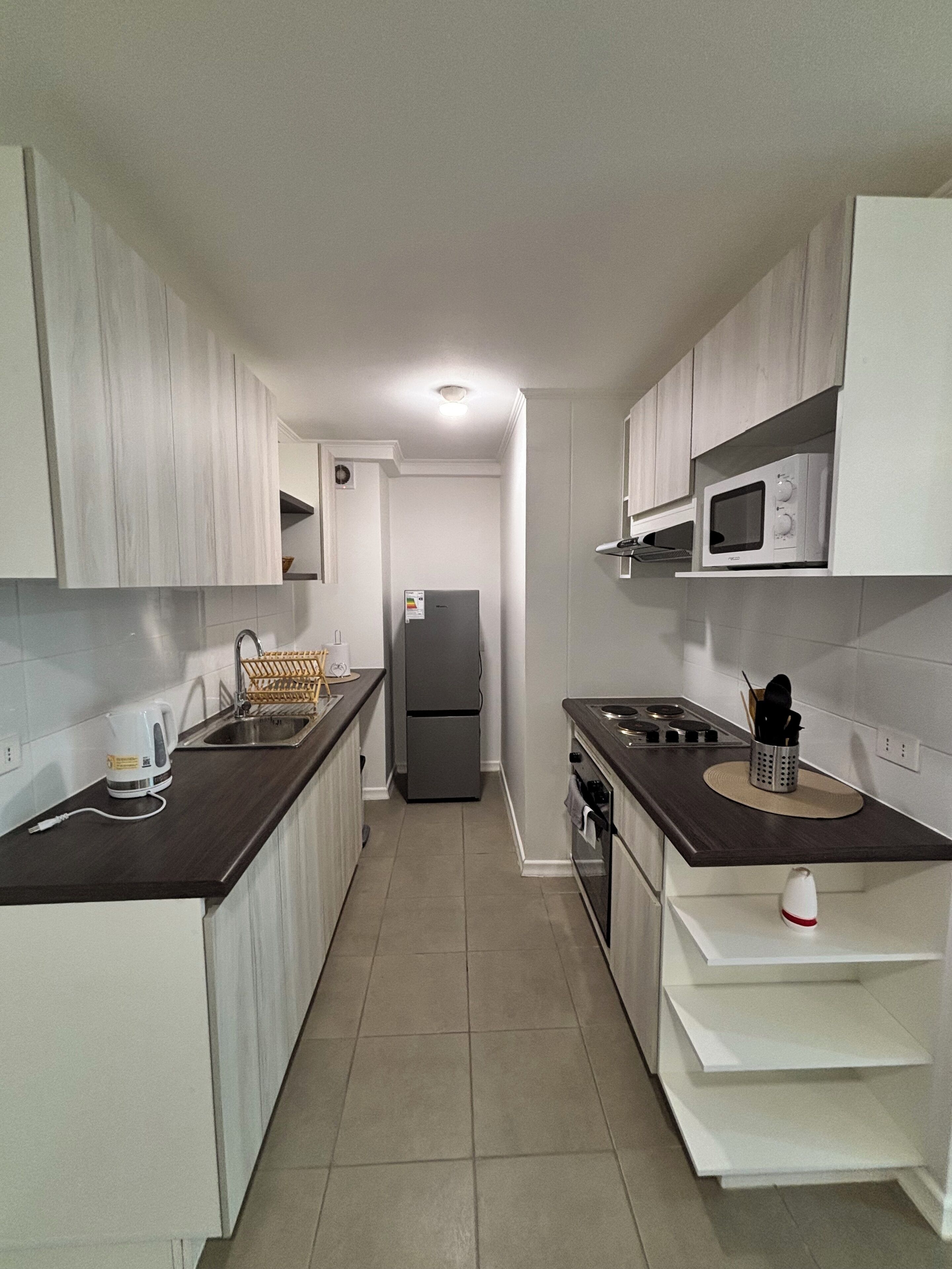 A narrow kitchen with white cabinets, a microwave, a refrigerator, and a stove.