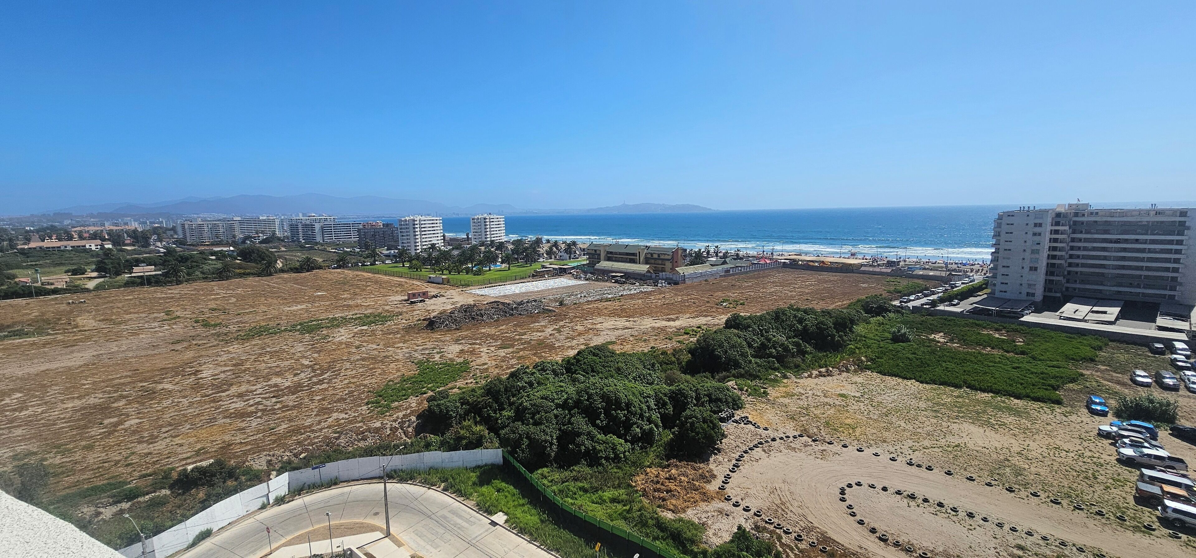A coastal view with a parking area, buildings, and a beach.