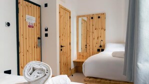 A hotel room with wooden doors, a bed, a small wooden nightstand, and a towel on the bed. - EasyHotel Paddington (London)