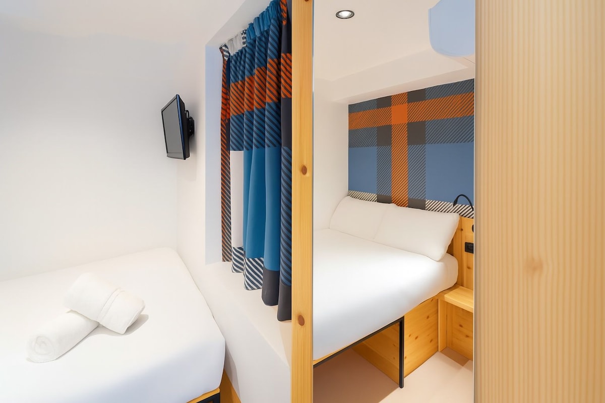 Een compacte kamer met een bed, een zithoekje, een televisie en een kamer met een patroon.