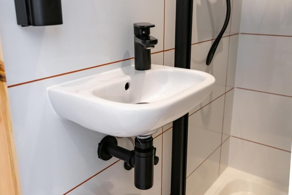 A white bathroom sink with a black faucet, mounted on a tiled wall with a wooden panel on the left.