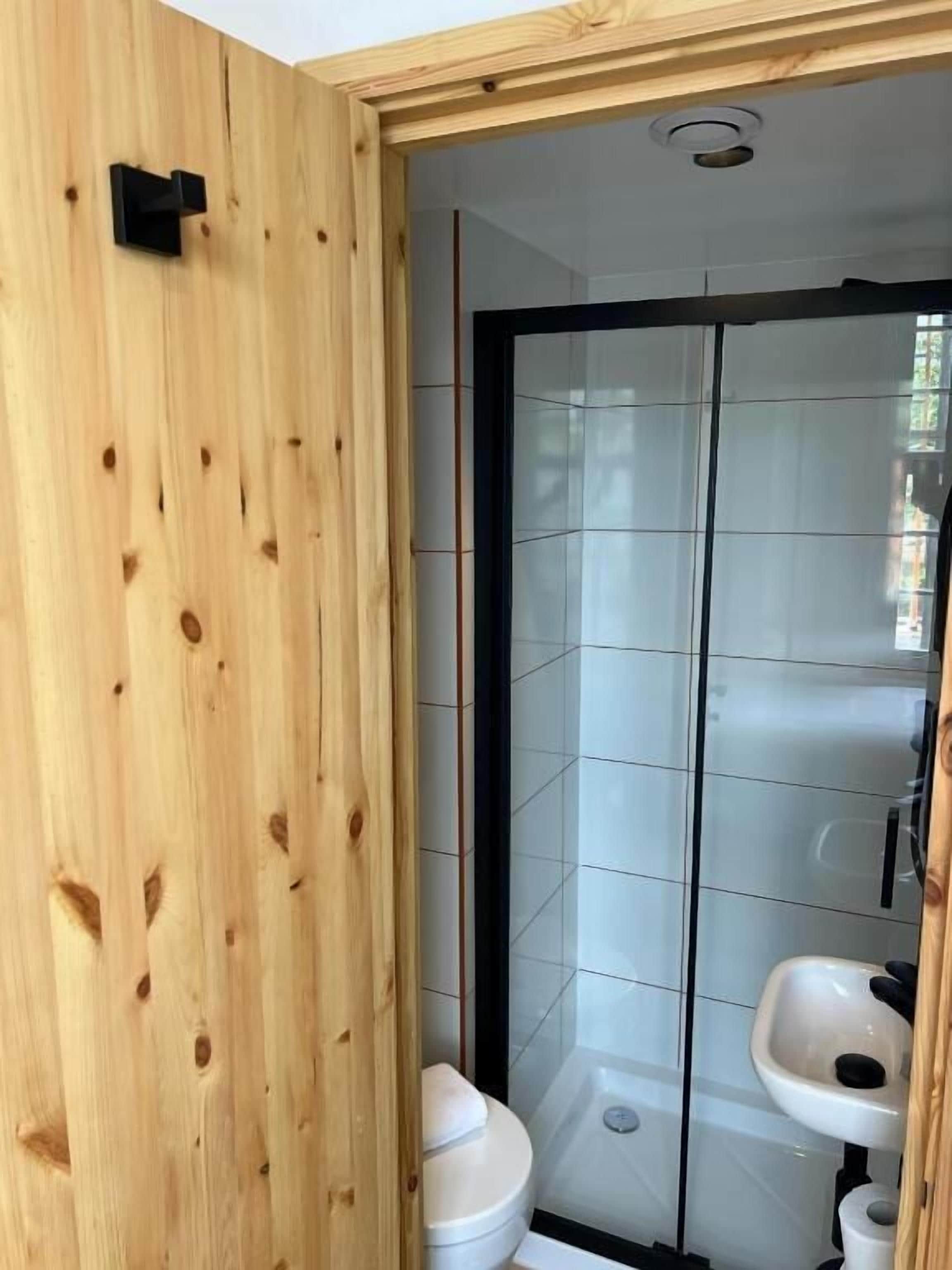 A bathroom with a wooden wall, a glass shower enclosure, a toilet, and a sink.