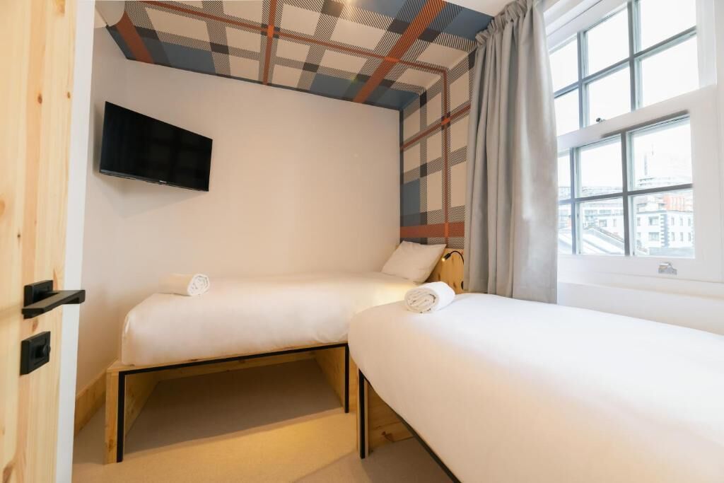 Une chambre d’hôtel avec deux lits simples, un téléviseur à écran plat fixé au mur et une fenêtre avec des rideaux.