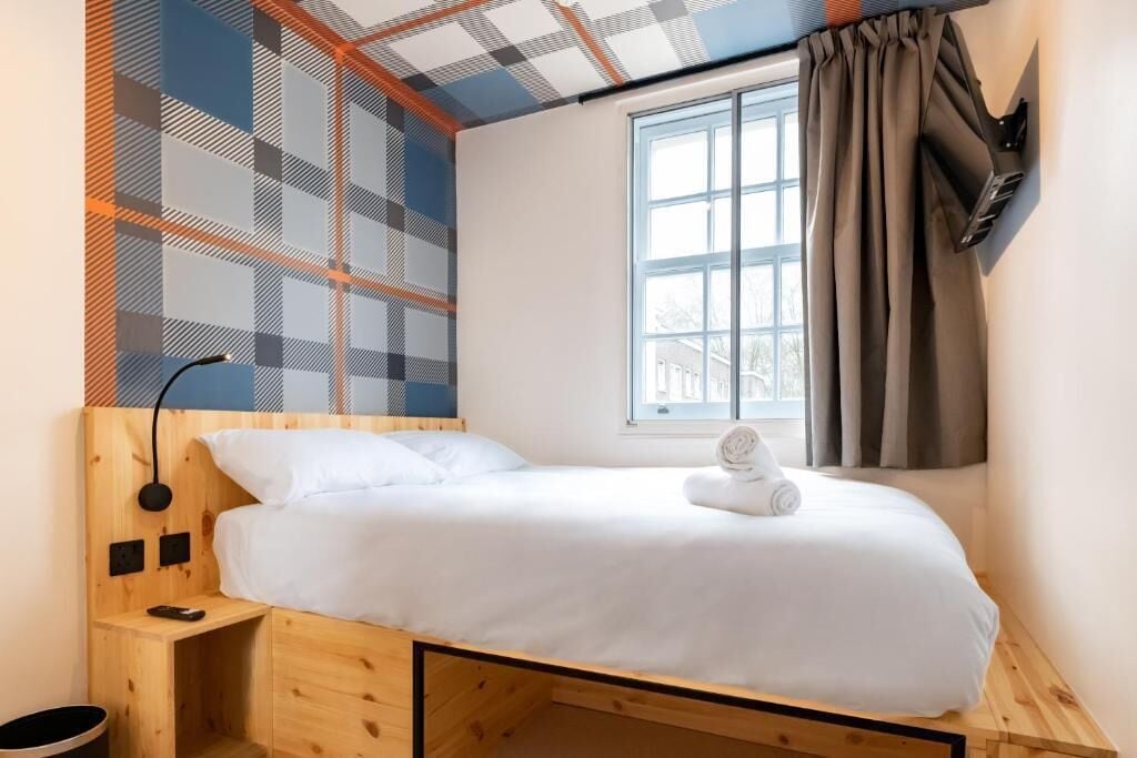 A single bed with a wooden headboard, a bedside table with a lamp, and a window with curtains.