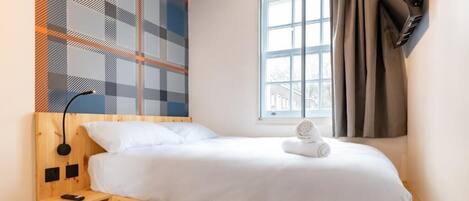 A single bed with a wooden headboard, a bedside table with a lamp, and a window with curtains.
