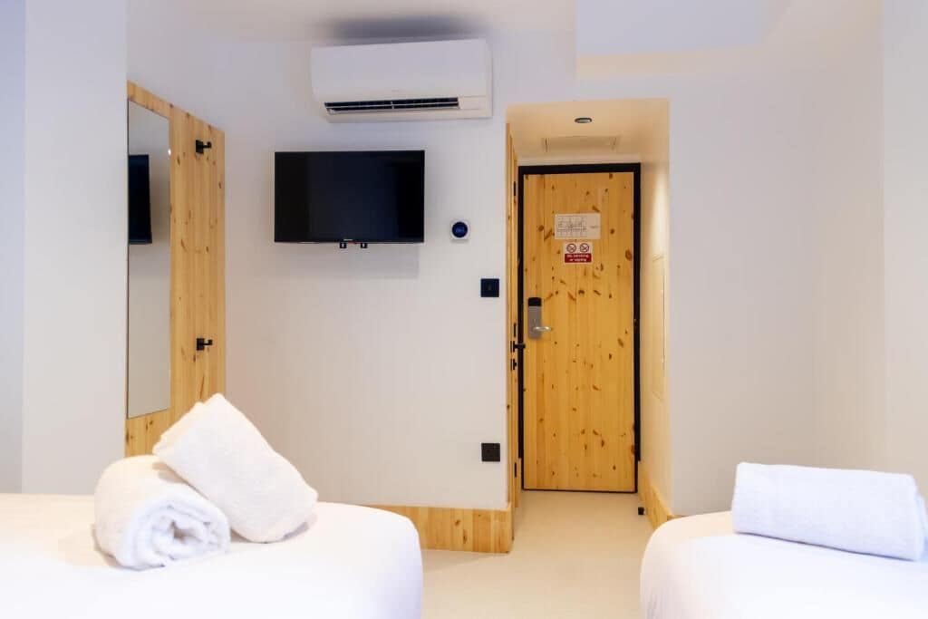 A hotel room with a wooden door, a mounted TV, and two beds with rolled white towels.
