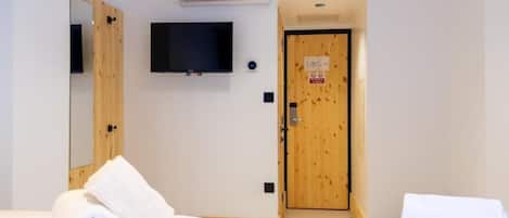 Une chambre d’hôtel avec une porte en bois, un téléviseur fixé au mur et deux lits garnis de serviettes blanches pliées.
