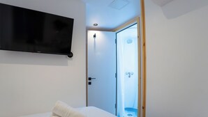 A bedroom with a bed, a television mounted on the wall, a shower, and a door leading to another room. - EasyHotel Paddington (London)