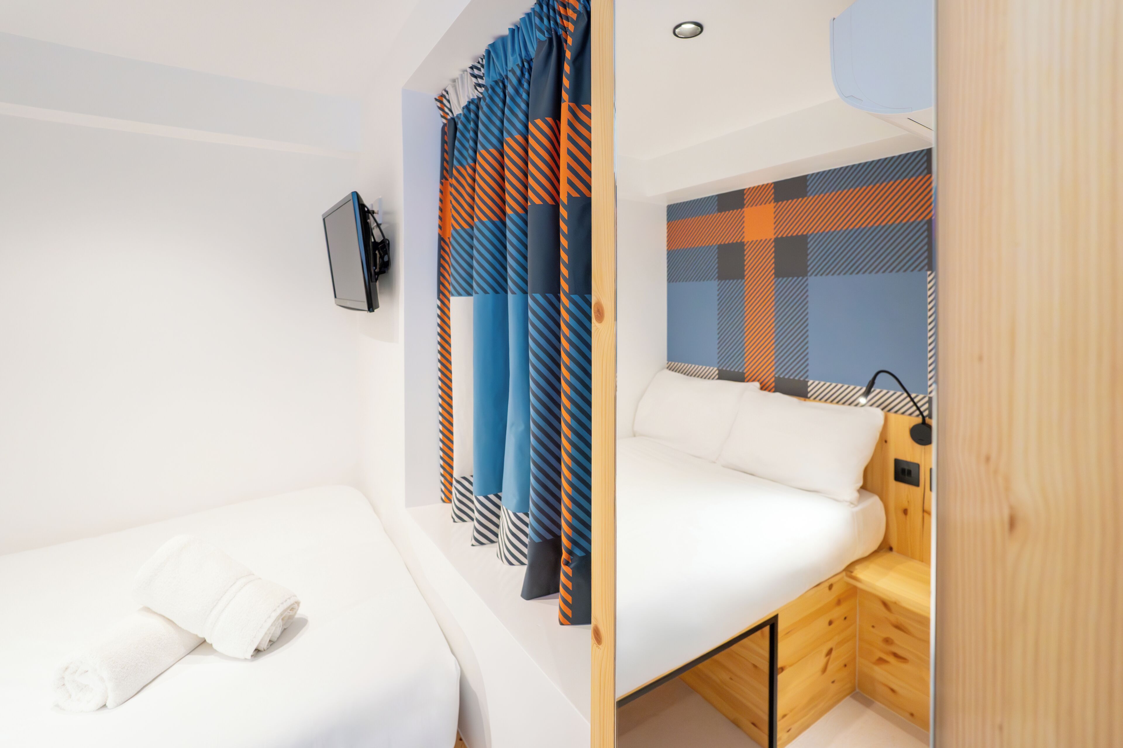 A modern bedroom with a bed, a small seating area, a TV, and a patterned curtain.