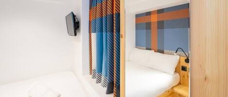 A small, modern room with two beds, a wooden bench, and a TV mounted on the wall.