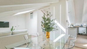 A modern living space with a glass dining table, white sofa, and a plant in a vase. - Como Sky Suite by Rent All Como (Como)