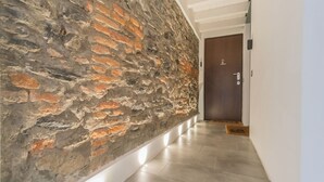A hallway with a textured stone wall and a wooden door at the end. - Como Sky Suite by Rent All Como (Como)