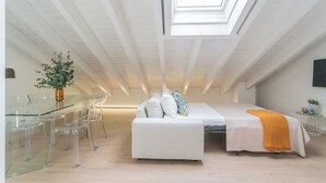 A modern loft bedroom with a skylight, a glass dining table, and a white sofa. - Como Sky Suite by Rent All Como (Como)