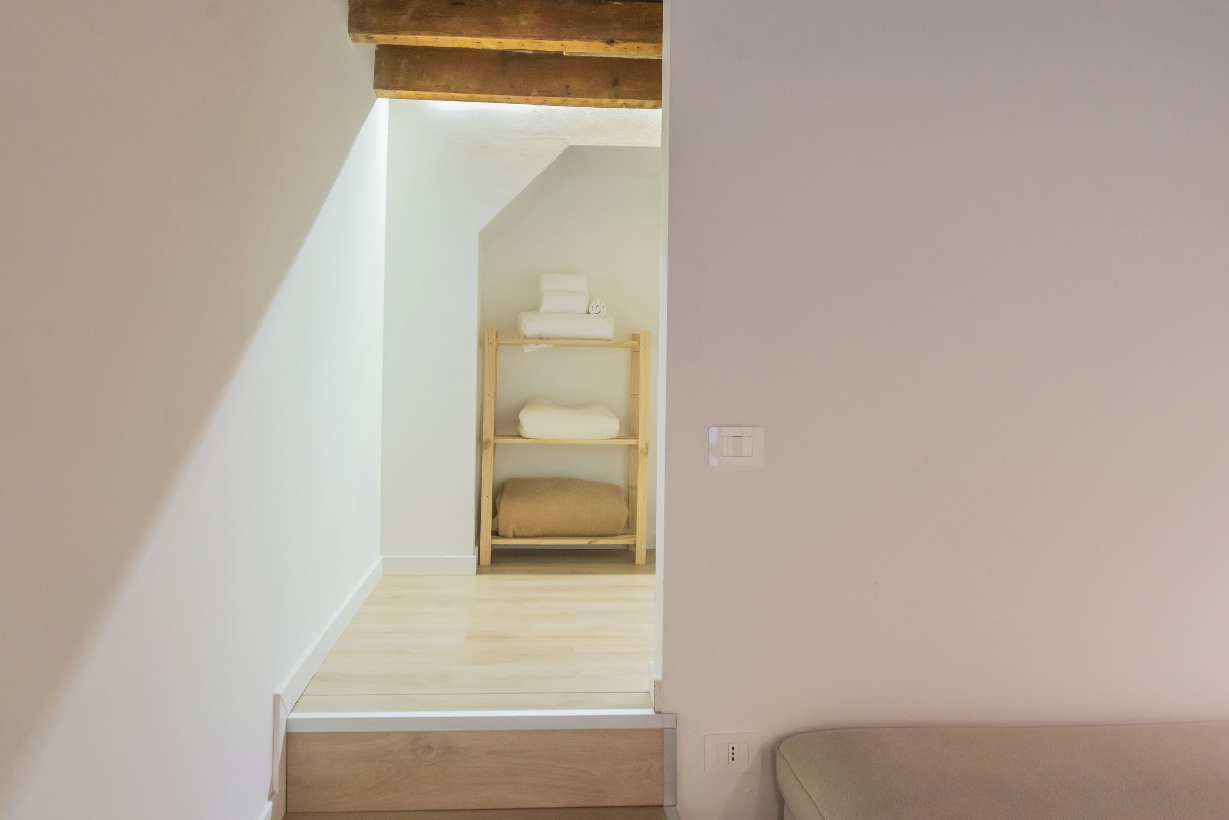 A narrow hallway with wooden flooring and a wooden bench at the end.