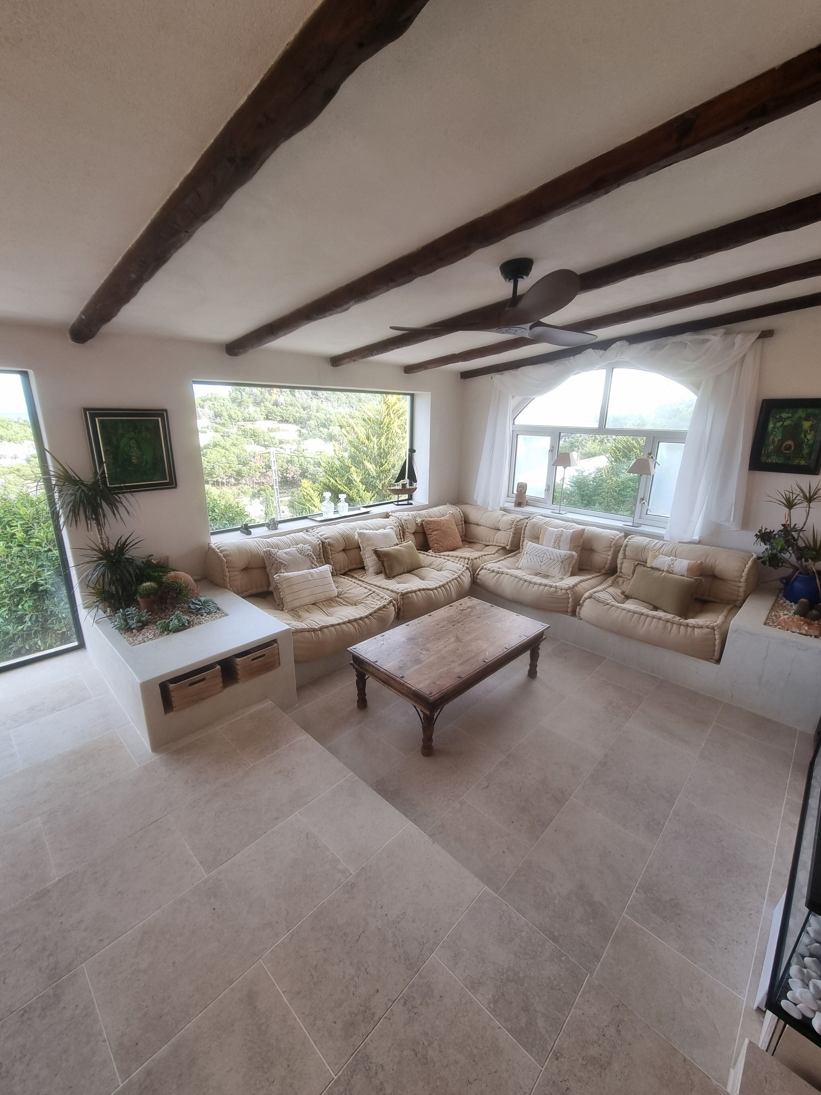 A spacious living room with a large sectional sofa, a wooden coffee table, and a view of greenery through large windows.