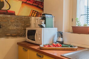 Une cuisine équipée d’un four à micro-ondes, d’une machine à café et d’une planche à découper avec des tomates et des concombres.