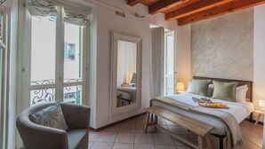 Een slaapkamer met een bed, een bankje, een stoel en een groot raam.