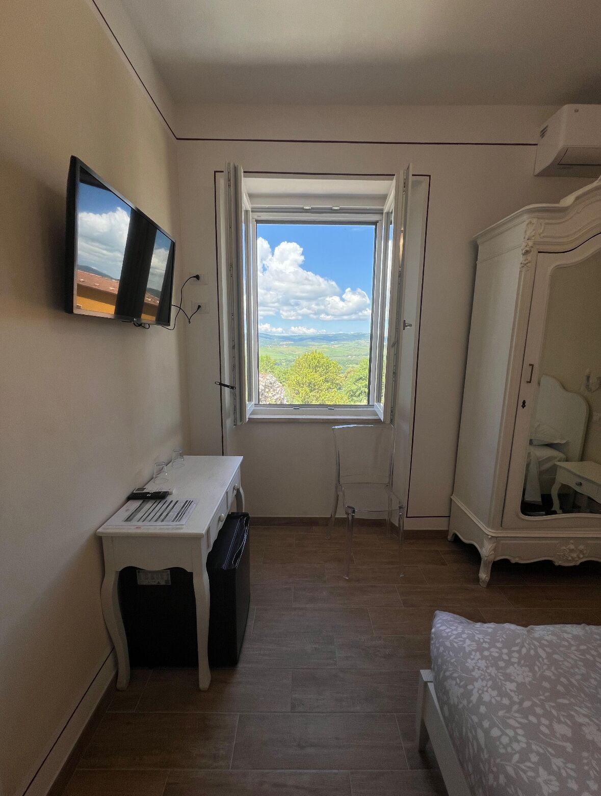 Een slaapkamer met een bureau, een bed, een kledingkast en een raam met uitzicht op groen.
